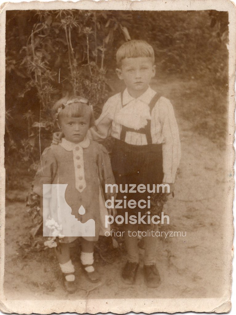 Na pierwszym planie fotografii dwoje małych dzieci Jaś i Krysia Śliwińscy. W tle ogród.