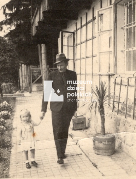 Ojciec prowadzi za rączkę kilkuletnią dziewczynkę. Spacerują wzdłuż domu w Grieskirchen.